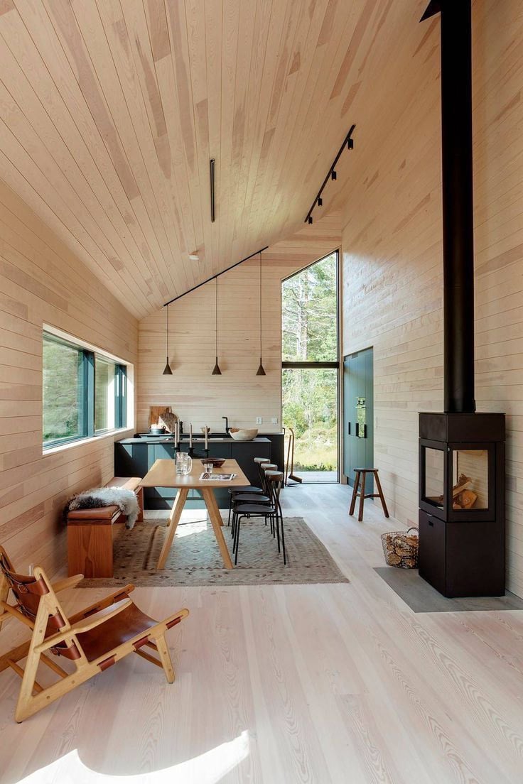Espacio integrado de living y comedor revestido en madera clara, con doble altura y estufa a leña